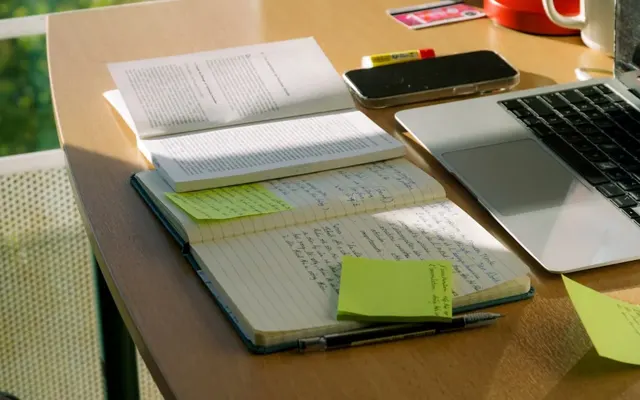Laptop and handwritten notes on a sunlit desk