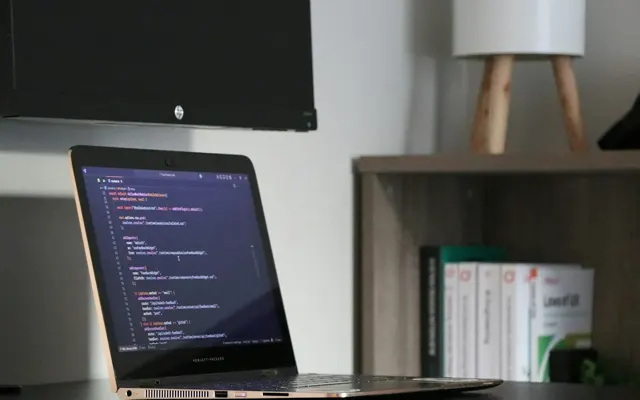 Laptop displaying code beside bookshelves